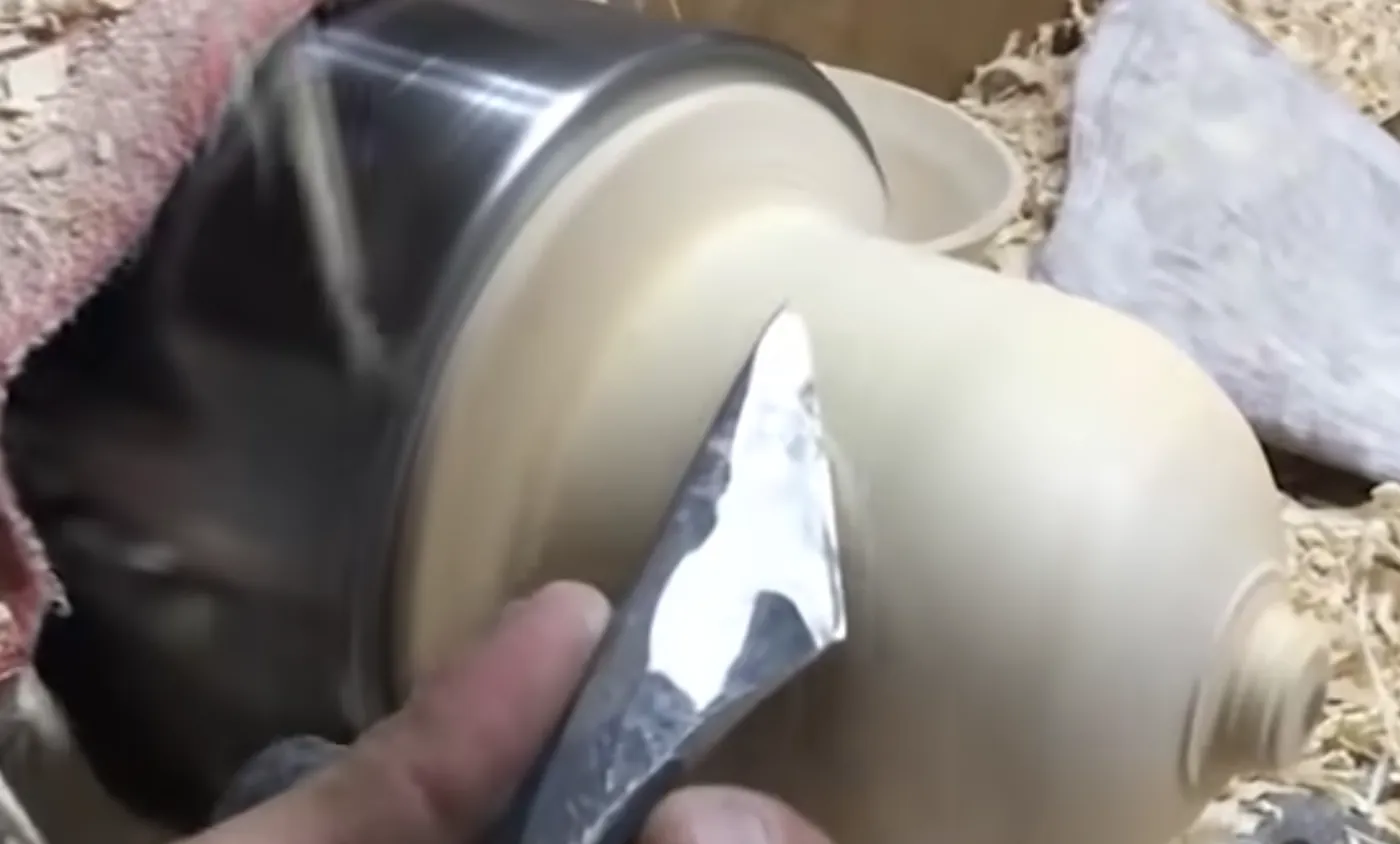A forged lathe knife shaping the curve of a pale turned vase on the lathe